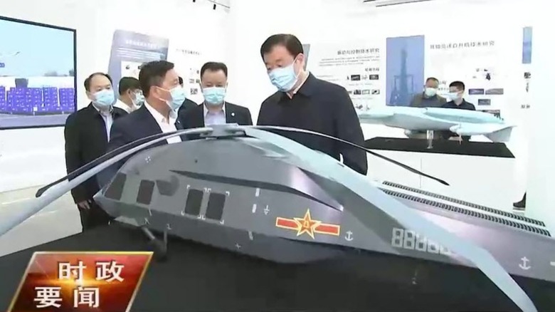 Men in surgical masks viewing a model of what may be the Chinese Z-20 stealth helicopter.