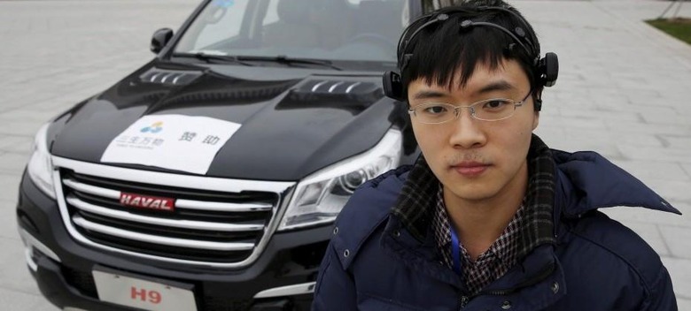 Researcher Zhang Zhao wearing a brain signal-reading equipment poses with a vehicle which can be controlled with his brain wave, during a demonstration at Nankai University in Tianjin