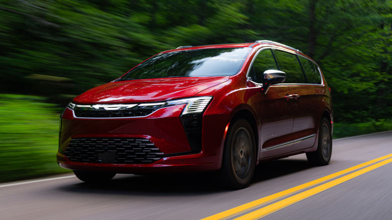 A red 2027 Chrysler Pacifica Pinnacle driving on a road lined with trees.