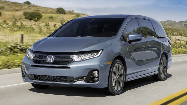 A blue-gray 2026 Honda Odyssey driving on a country road