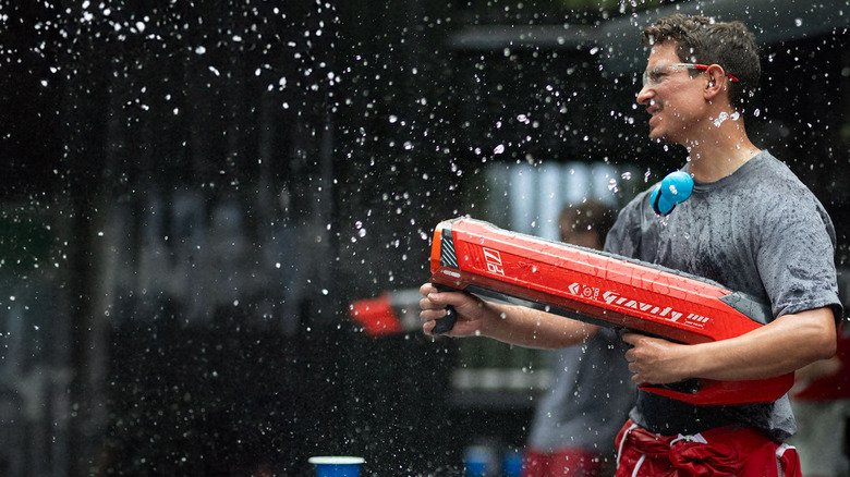 Man holding red water gun with water spraying around him