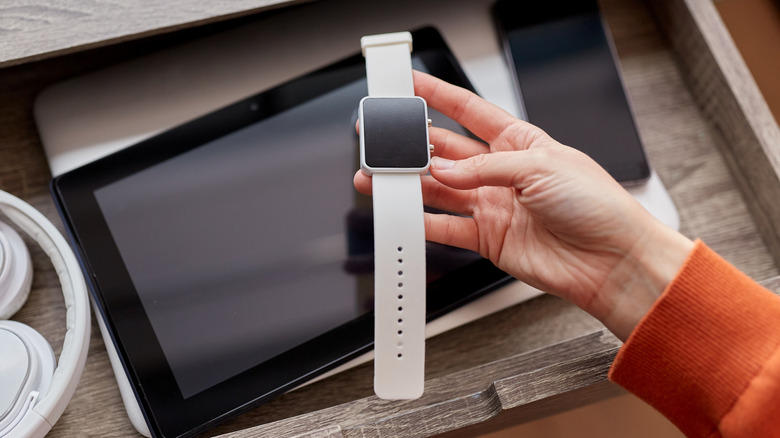 digital detox and technology concept - close up of hand holding smart watch and different gadgets in desk drawer at home