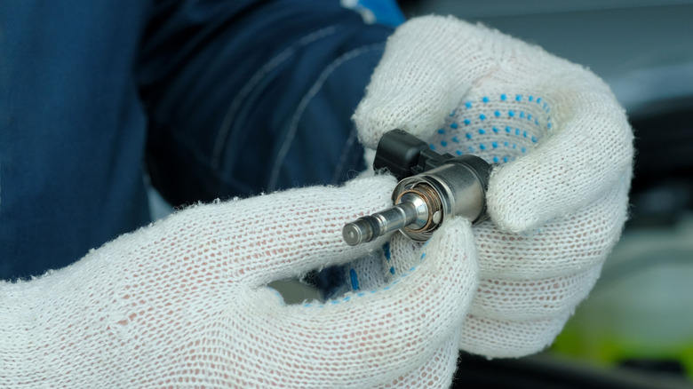 car mechanic holding a fuel injector in his hand