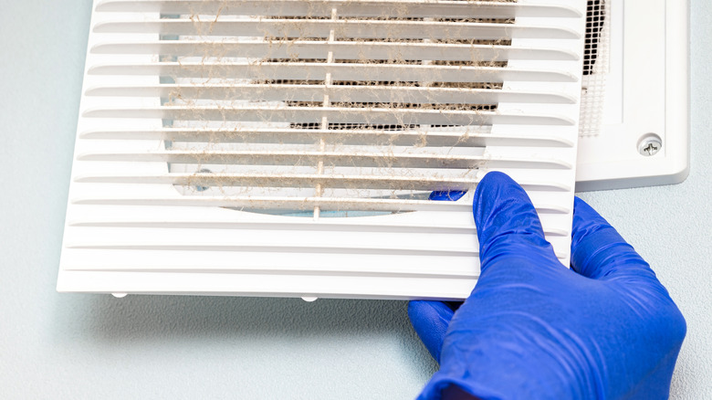 A person removing a dirty vent grill