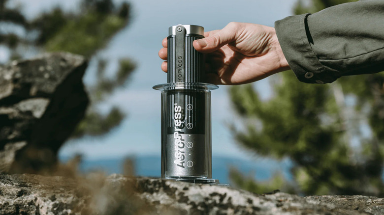 An aeropress manual coffee grinder inside of an aeropress machine placed on rocks outside.