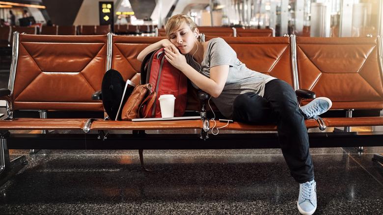 A woman sleeping, leaning on her bag, in an airport's boarding lounge.