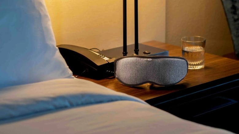 The Lumos sleeping mask sitting on a cabinet, next to a bed.