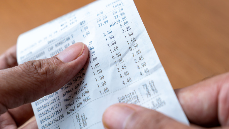 A person's hands are holding up and examining a long printed grocery receipt.