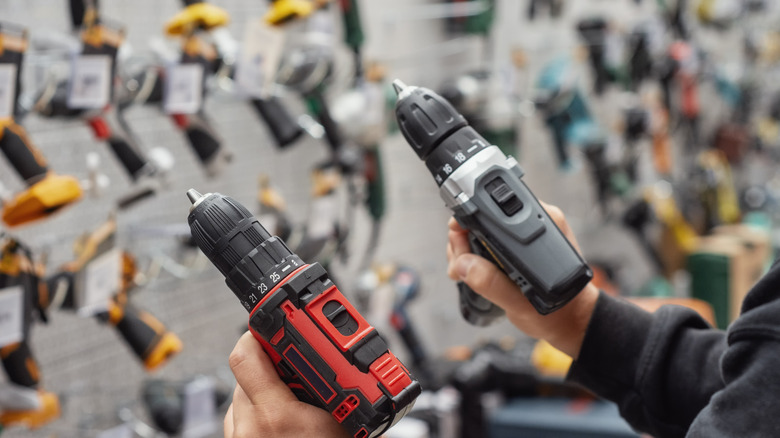 A person holding two cordless drills in a hardware store.