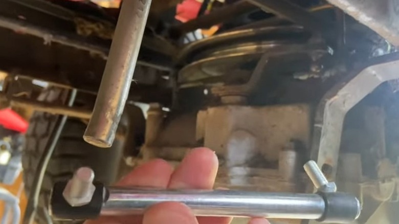 A broken shifter linkage and its replacement under a Craftsman riding mower.