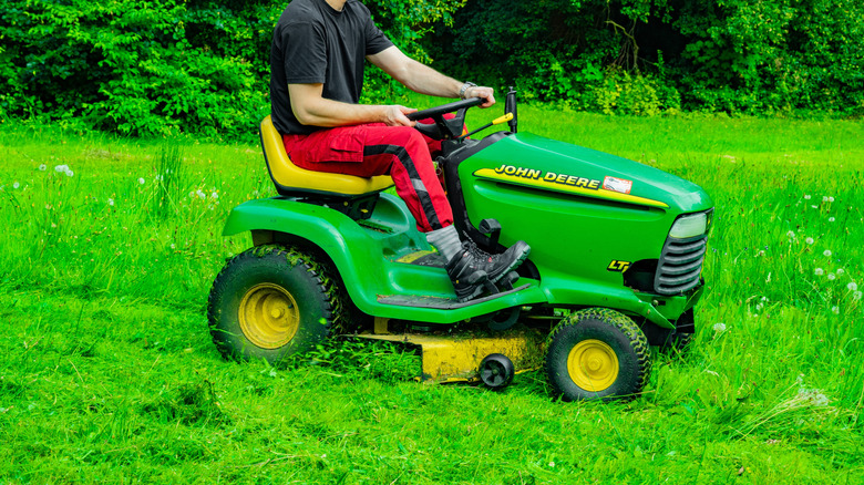 Man in red pants cutting lawn on John Deere riding mower