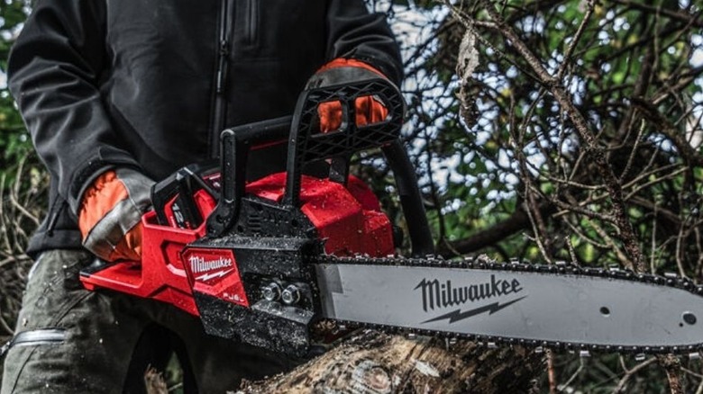 A man cutting a log with a Milwaukee Cordless Chainsaw