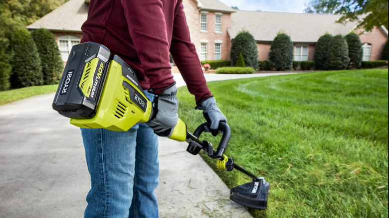 A man trimming lawn with a Ryobi 40V string trimmer