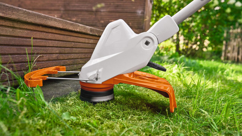 A Stihl string trimmer trimming grass along the edge of a deck.