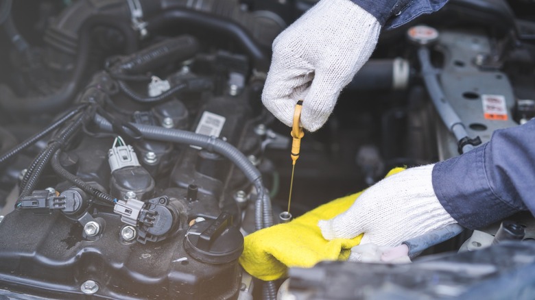 gloved hands checking engine oil dipstick