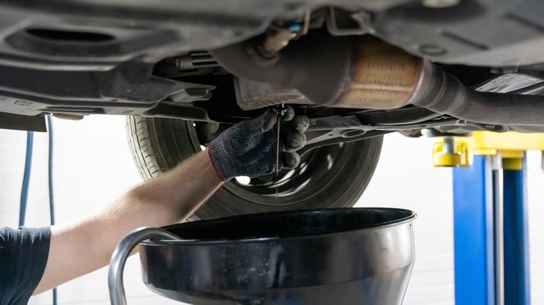 A mechanic drains oil from the oil pan of a car