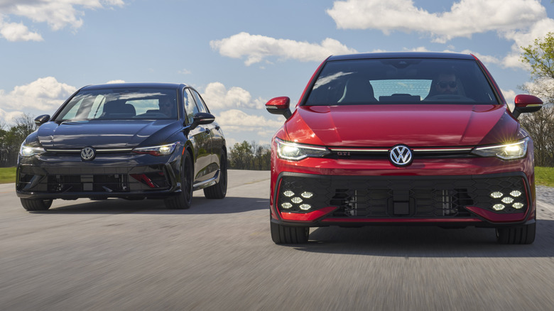 Front view of 2025 Golf R Black Edition (Mythos Black Metallic) and 2025 Golf GTI Autobahn (Kings Red Metallic) driving side by side