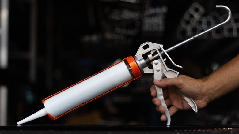 A close up of a hand holding a caulking gun