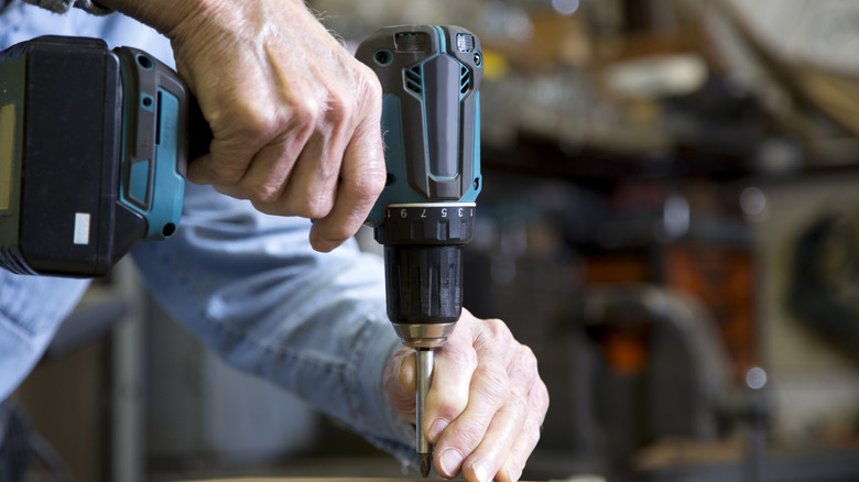 A person using an unbranded cordless drill on a wooden block