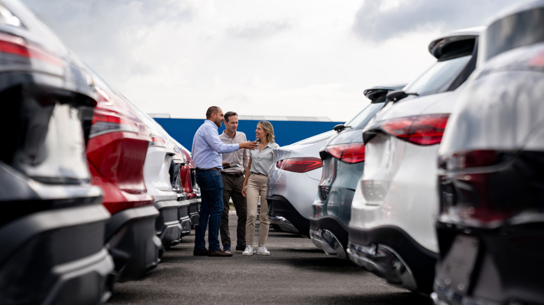 A couple standing with a salesman in between two rows of cars