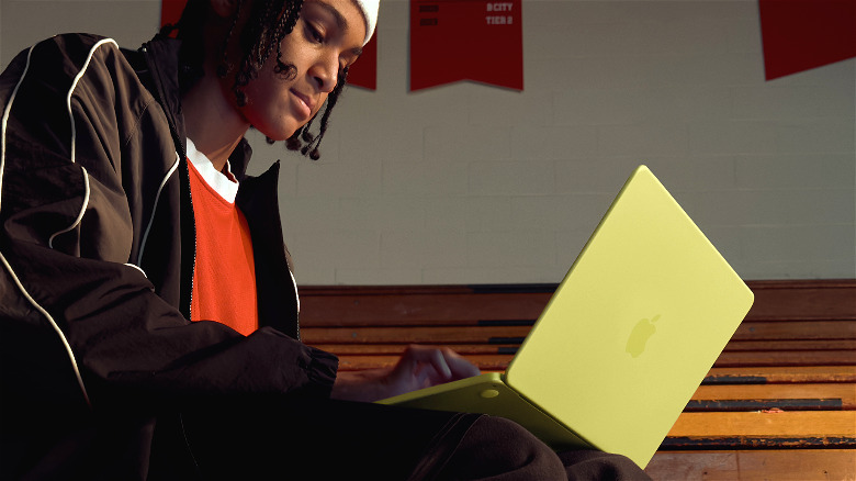 A young person using a yellow MacBook Neo in a gym.