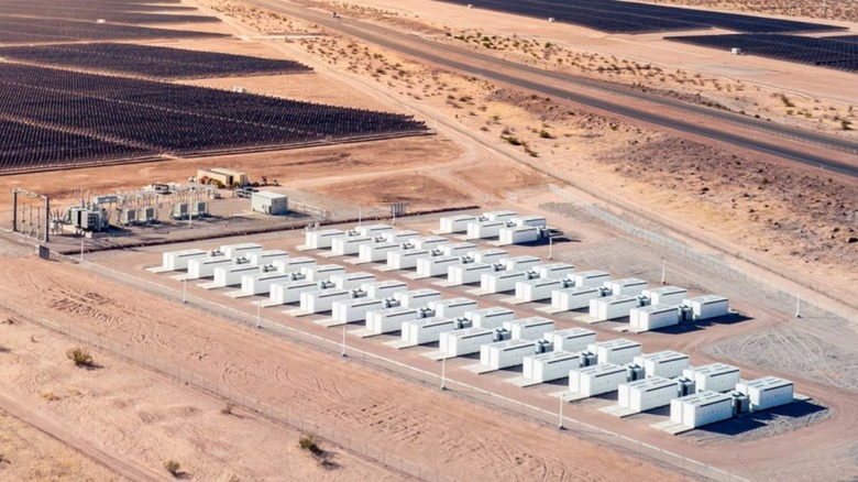 A renewable-energy installation using a large array of solar panels and 57 Tesla Megapacks on a desert landscape.