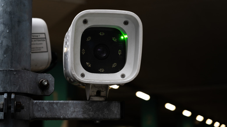 An automatic license plate reader camera posed towards the camera in a lit tunnel.