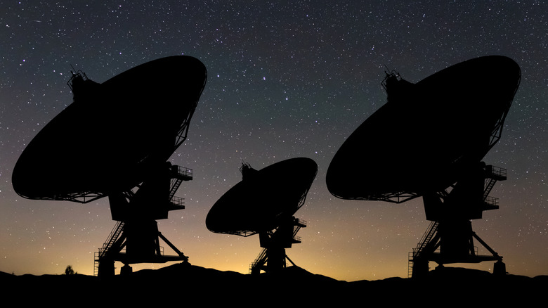 The silhouette of three radio antennas under a night sky