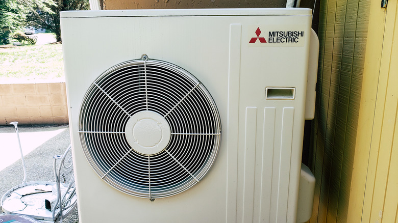 Close-up of a Mitsubishi compressor on the ground outside a home, next to a small chair