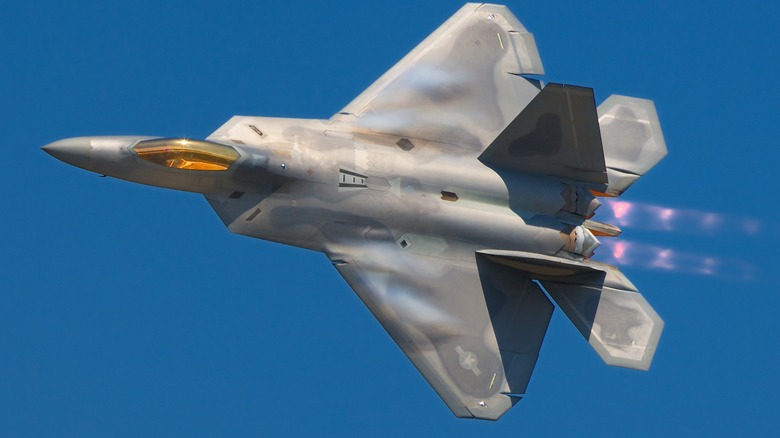 A Lockheed Martin F-22A Raptor with its afterburners engaged over a blue sky