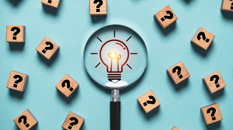 Glass magnifying a cartoon lightbulb with question marks surrounding it