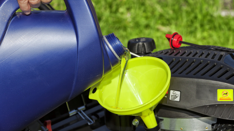 A person pouring oil into a lawn mower.