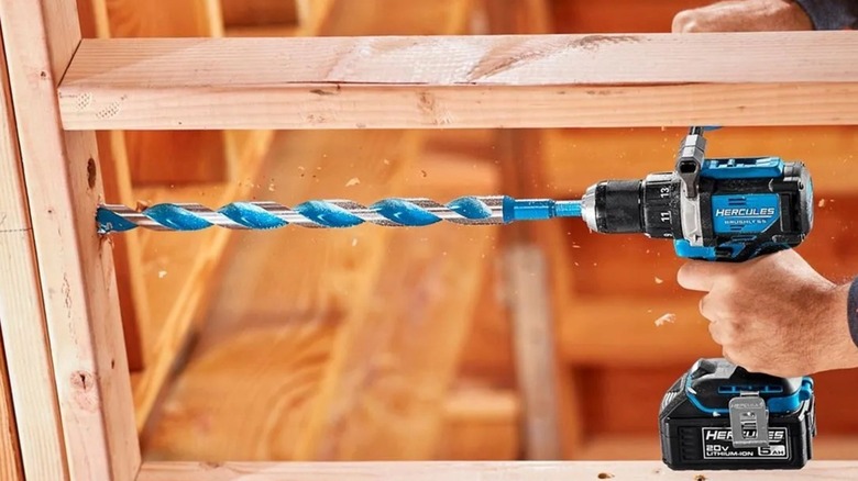 Man drilling hole in wood framing using Hercules drill and long bit