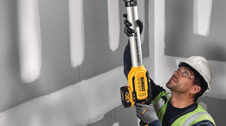 Worker using DeWalt Drywall Sander on grey ceiling