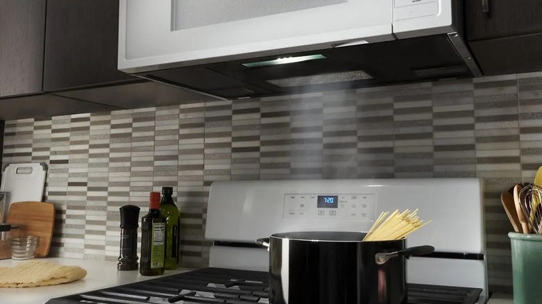 Microwave showing grease filters under and pasta cooking on stovetop below