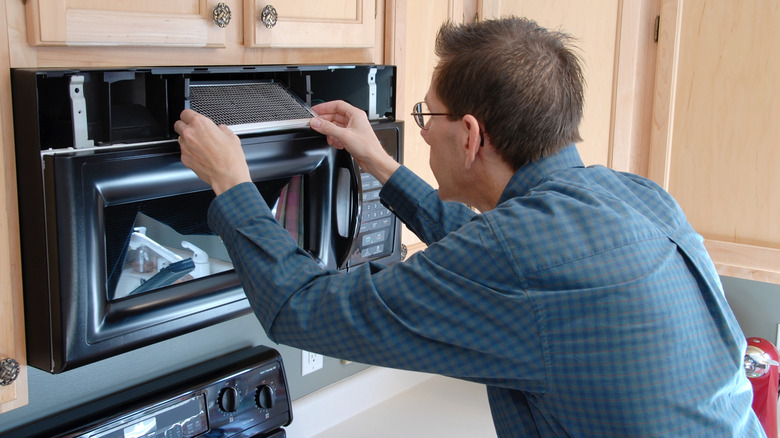 Man removing charcoal filter from over-the-range microwave in kitchen