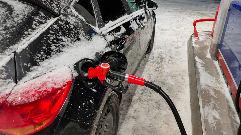 Žiemos naktį degalinėje pildosi apsnigtas juodas automobilis
