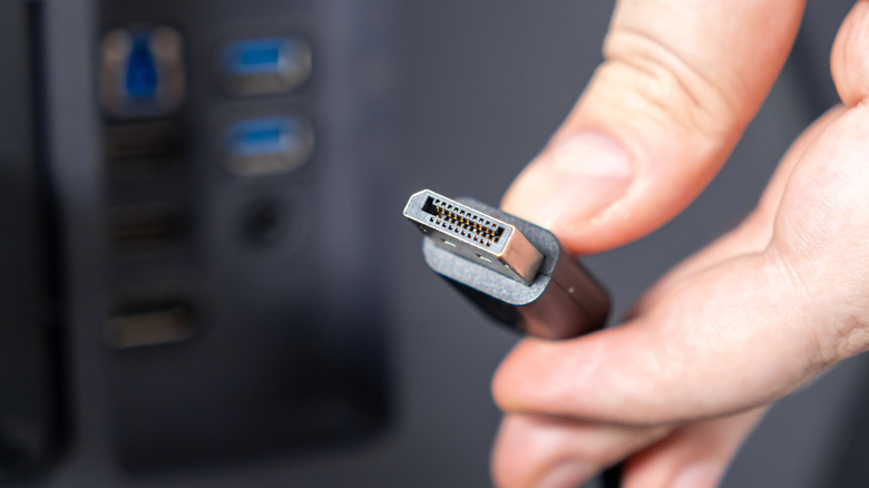 A person holds a DisplayPort cable in their hand next to a DP port