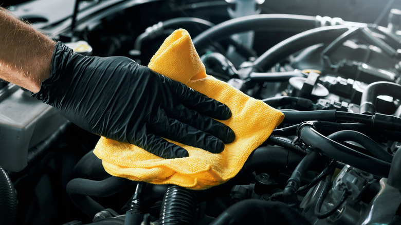 Mechanic cleaning car engine with yellow microfiber cloth