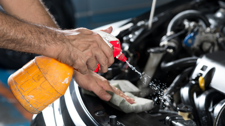 A guy cleaning car engine with spray-on cleaner
