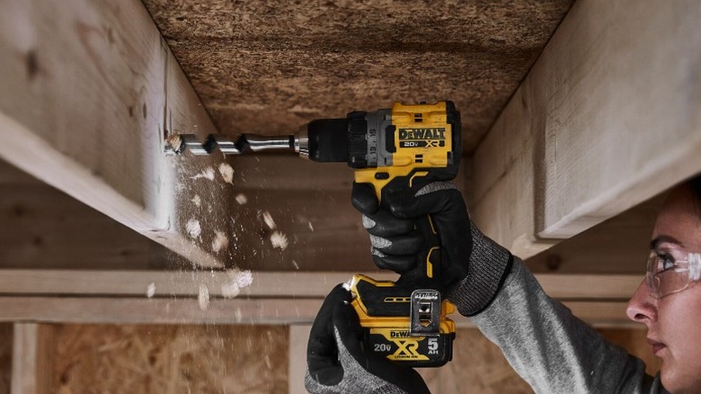 Person drilling into a floor joist with a DeWalt drill