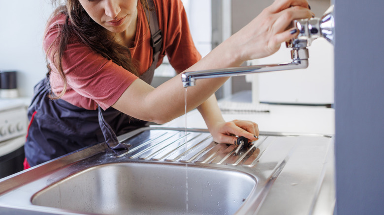 A woman fixing a drain and holding a screwdriver