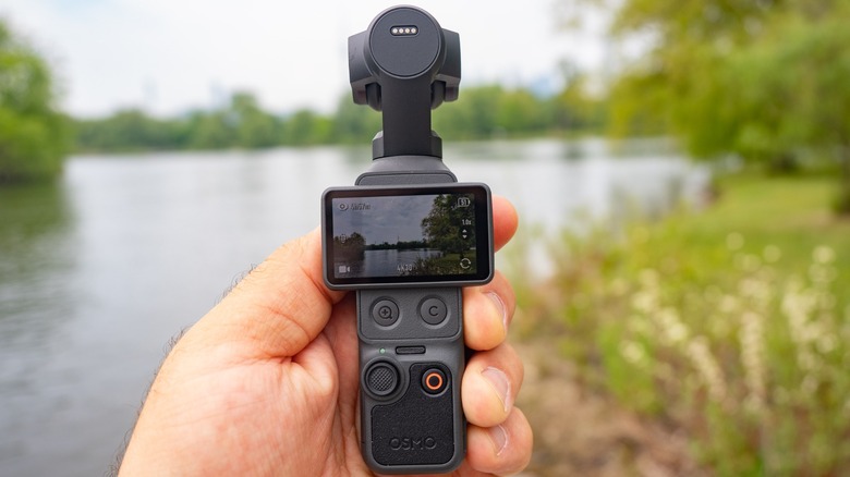 The DJI Osmo Pocket 4 held in a hand with an out of focus landscape in the background.