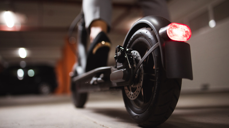 Feche as pernas e os pés da mulher em pé na scooter elétrica