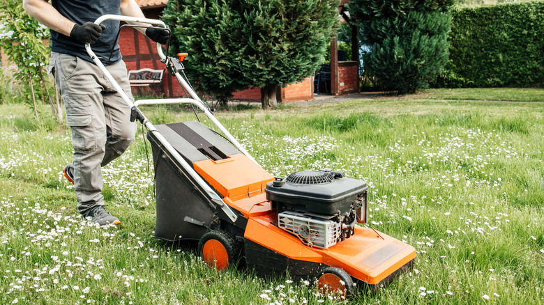 A man mowing grass with an orange and black land mower