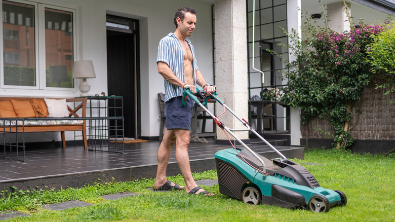 A man wearing open shirt maintaining his lawn using a lawn mower