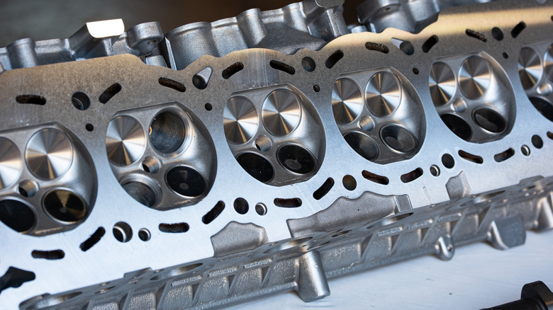 An angled close-up of machined combustion chambers and engine valves in an aluminum six-cylinder head