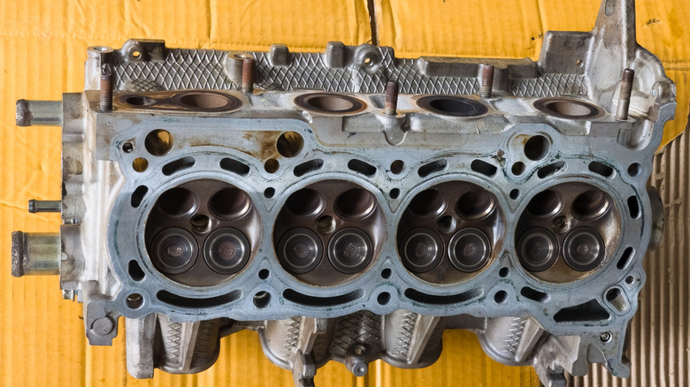 Close-up of a disassembled four-cylinder aluminum engine cylinder head showing combustion chambers and valves on cardboard background