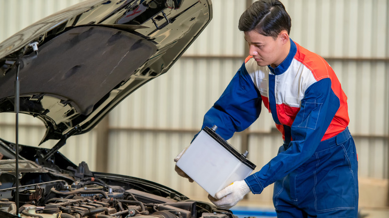 A mechanic in a blue, red, and white suit installing a new car battery
