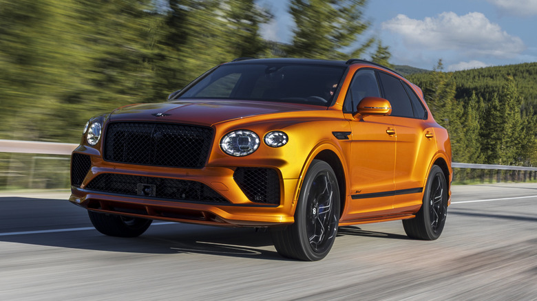 A bright orange Bentley Bentayga driving on the road surrounded by trees